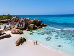 Couple walking along stunning Seychelles beach with rock formation