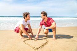 2 gay men drawing a heart on beach while visiting LGBT friendly holiday destinations