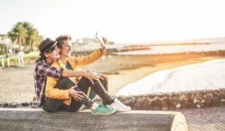 Gay couple taking selfie on beach visiting LGBT friendly holiday destinations.