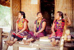 3 women dressed in traditional Alak dress sit on front step of building